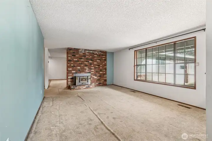 View of the living room from the hallway, double-sided fireplace and kitchen straight ahead. Love the large windows!