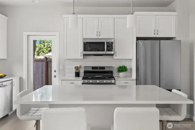 A vision in white—counters, tile, and cabinetry blend seamlessly for a crisp, modern aesthetic, subtly contrasted by the sleek elegance of stainless steel appliances