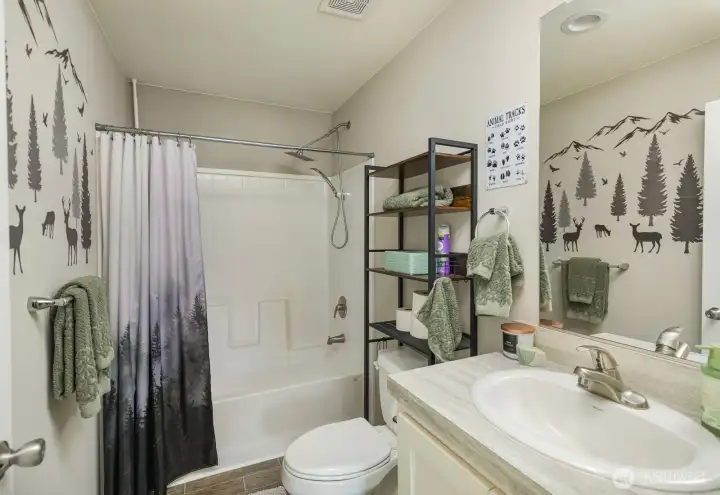 A clean and well-designed full bathroom with tub/shower combo, modern fixtures, and playful nature-themed wall accents for added charm.