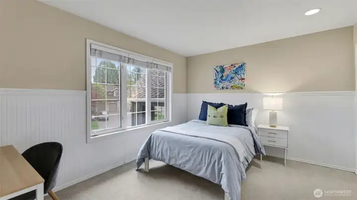 Spacious secondary bedroom with wainscoting and overhead lights.