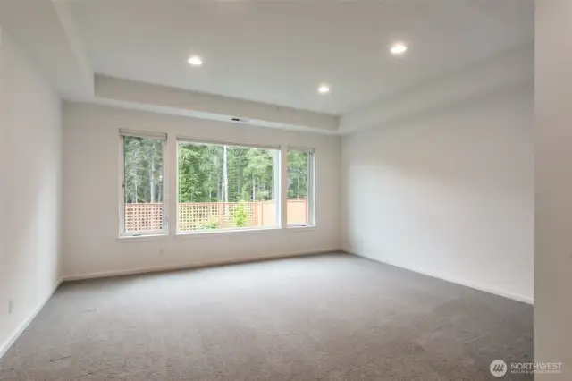 Primary bedroom with coffered ceiling and plenty of windows with view of greenbelt
