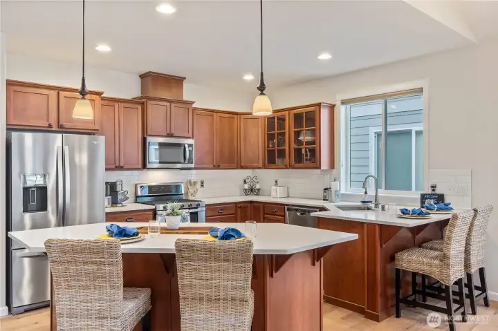 Stainless-steel appliances and a generous island with seating make meal prep and casual dining a joy. Pendant lighting and large windows bathe the space in natural light, creating a welcoming atmosphere.