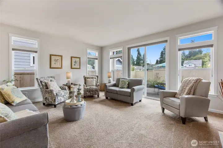 The adjacent dining area flows seamlessly into a comfortable living room with plush carpet and expansive windows, offering an easy connection to the backyard patio. Together, these spaces provide a perfect setting for daily living and effortless entertaining.