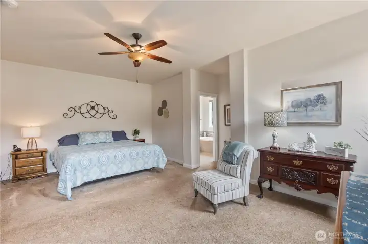 The primary bedroom offers a tranquil retreat with generous proportions and tasteful design. A neutral palette and plush carpeting create a soothing ambiance, while a ceiling fan adds comfort and complements the high ceiling.