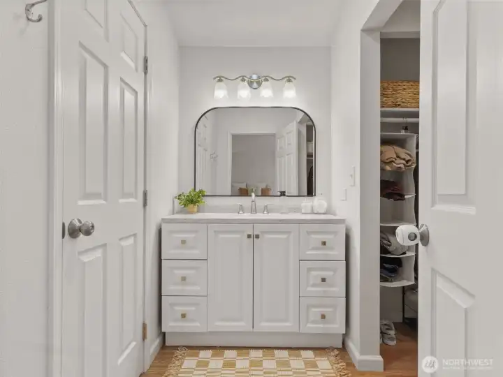 Primary bathroom vanity with walk-in closet at right and private toilet/shower space at left.