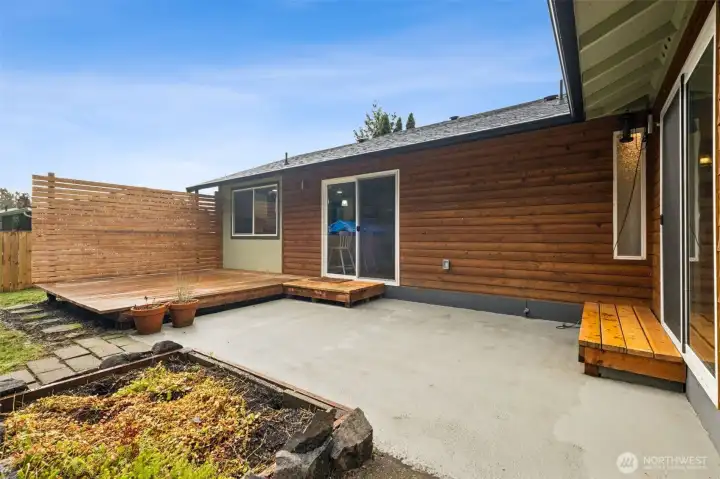 Combination of patio space and raised deck with privacy screen. Custom wood siding adds a modern touch to the home.
