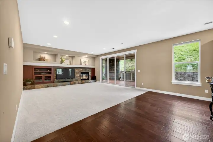 Inviting great room features new carpet, a cozy gas fireplace, built-in shelving with backlighting, and a slider leading to the covered patio with an additional fireplace—ideal for year-round indoor/outdoor living.