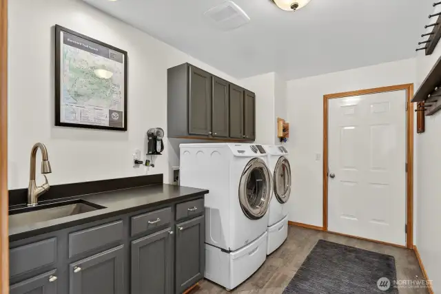 Large utility room with LVT flooring, granite counter top with utility sink and folding counter. Washer & dryer stay with the house. That door leads out to the garage.