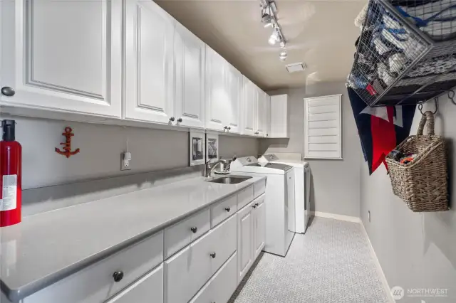 Spacious laundry room with a sink and long countertop is between the garage & kitchen
