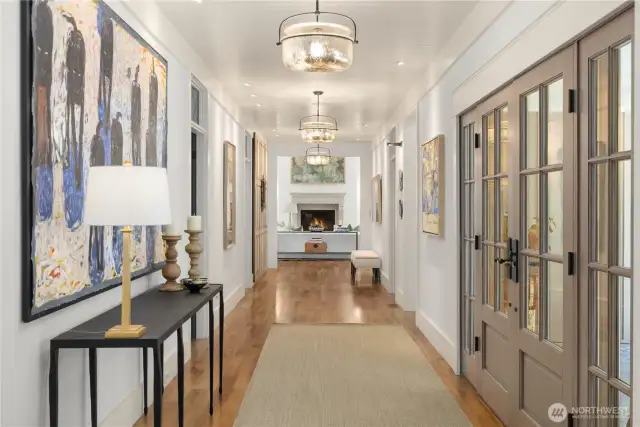 Grand center hall and gallery with freshly paneled walls and ceiling, art lighting, and glass transoms over doorways