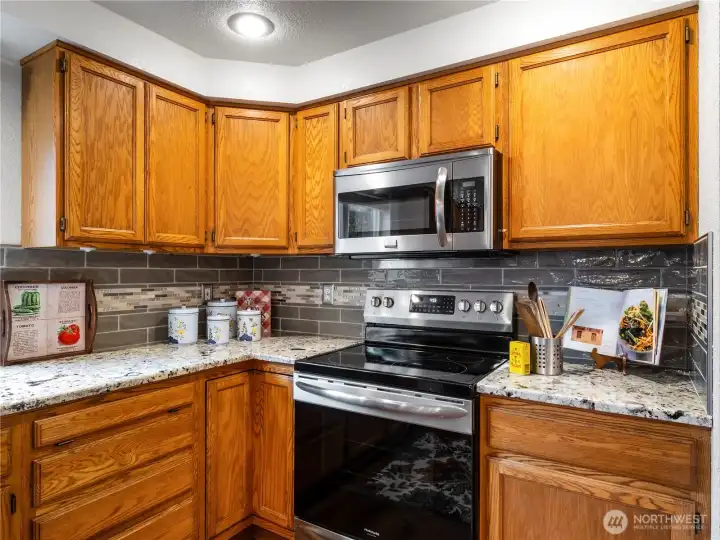 Beautiful glass tile back splash goes well with the warm wood and granite countertops.