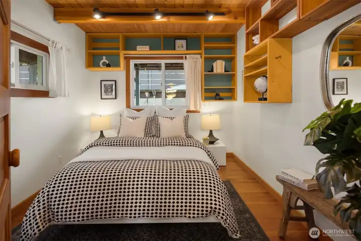 The main-level bedroom wraps you in wood beam ceilings and custom built-in shelving with backs painted in a calm teal, creating a cozy and personal retreat.
