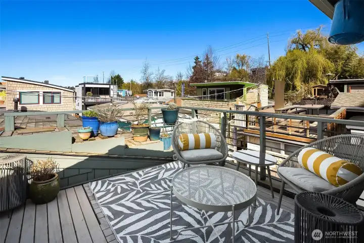 The rooftop deck is an outdoor room in its own right, with seating, potted plants, and panoramic views over the lake, surrounding floating home community and open sky.