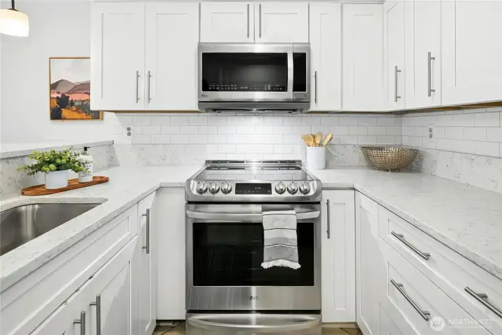 Updated kitchen boasts stainless steel appliances, white wood cabinetry, quartz countertops and a subway tiled backsplash.