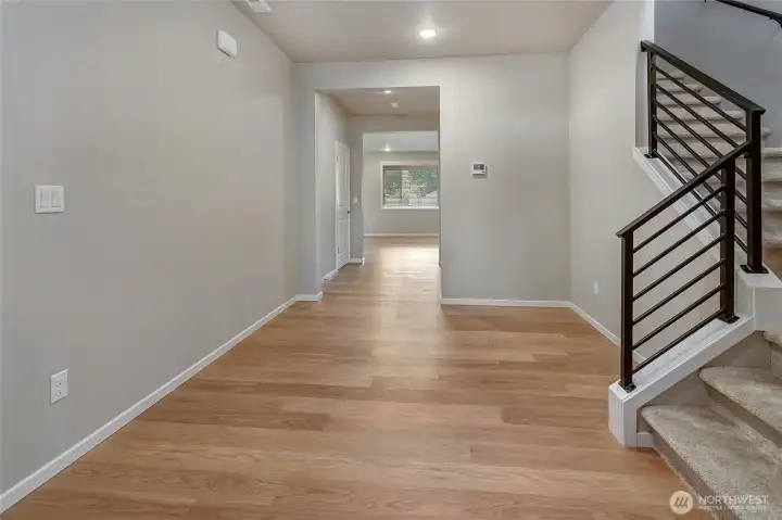 This wide, open entryway sets a modern tone with light wood flooring, soft gray walls, and recessed lighting that create a bright, welcoming atmosphere. A striking staircase with horizontal black metal railing adds architectural flair, while natural light enhances the spacious, thoughtfully designed layout.