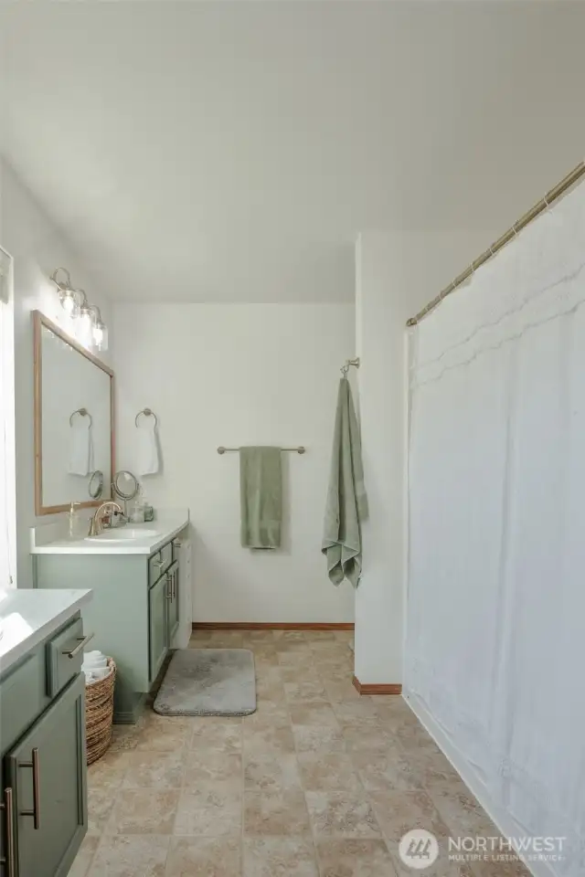 The primary bathroom, located just off the bedroom, features two separate vanities for added convenience, bright lighting throughout, and a full shower/tub combination—offering both comfort and functionality in a private, well-lit space.