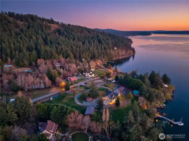 Stunning bird’s-eye view of the property’s waterfront setting at dusk, private deep-water dock, and forested surroundings