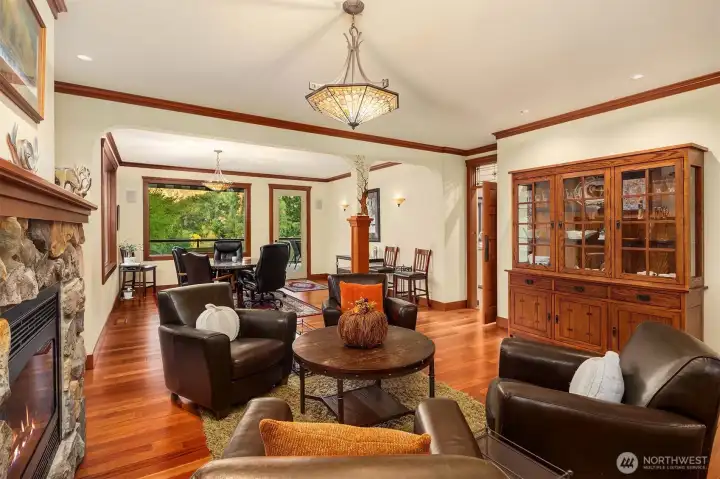 Light-filled sitting area with stone fireplace and rich wood details, seamlessly connecting to the dining space and capturing peaceful views beyond.