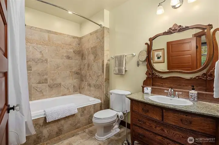 Primary bath with tiled tub/shower surround, granite vanity, and warm wood cabinetry, blending functionality with classic design.