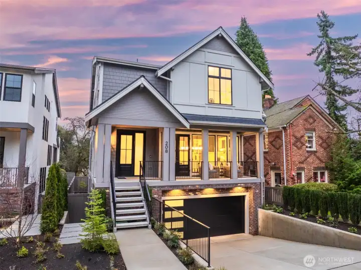 Striking front elevation with a covered porch, warm interior glow, and a drive-under two-car garage that gives this newly built home a polished, timeless presence.