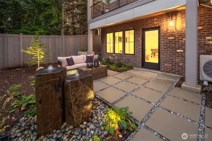 A closer look at the lower patio highlights the home’s curated outdoor experience, where fountain details, paver walkways, and warm evening light create a serene setting.