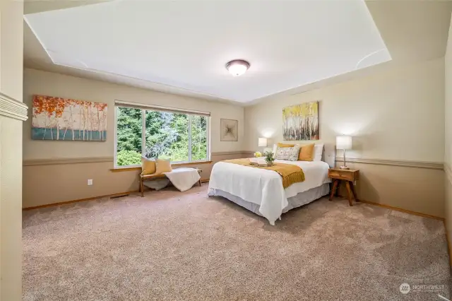 The dreamy primary bedroom boasts a stunning coffered ceiling and expansive windows offering picturesque views of the beautiful backyard.