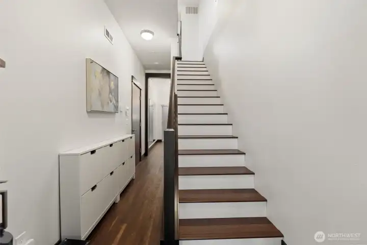 Bright entry foyer featuring hardwood flooring and a clean-lined staircase to the main living level.