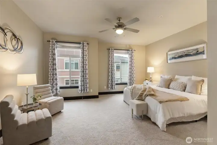 Spacious primary suite with plush carpet, ceiling fan, and large windows.
