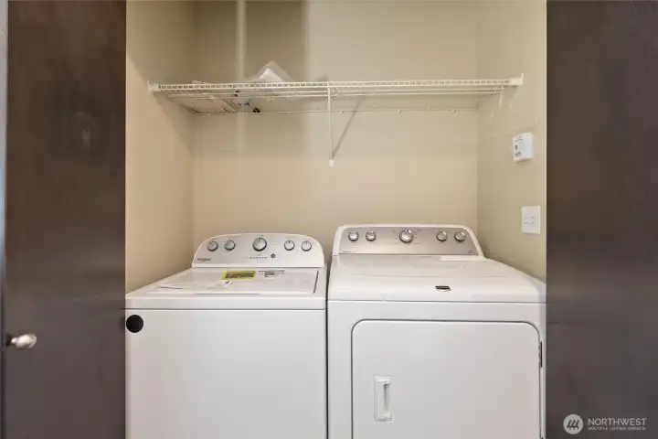 Dedicated laundry area with full-size washer and dryer and overhead shelving.