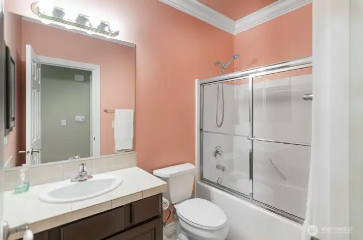 Hall bath with tiled countertops, crown molding, and glass tub/shower enclosure.