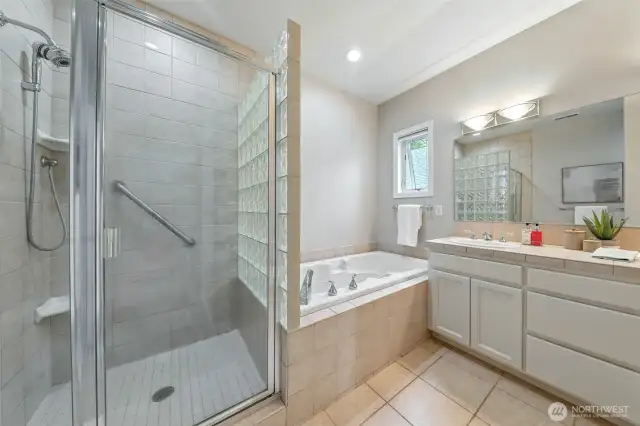 The primary bath features a jetted tub , glass shower and double sink vanity.