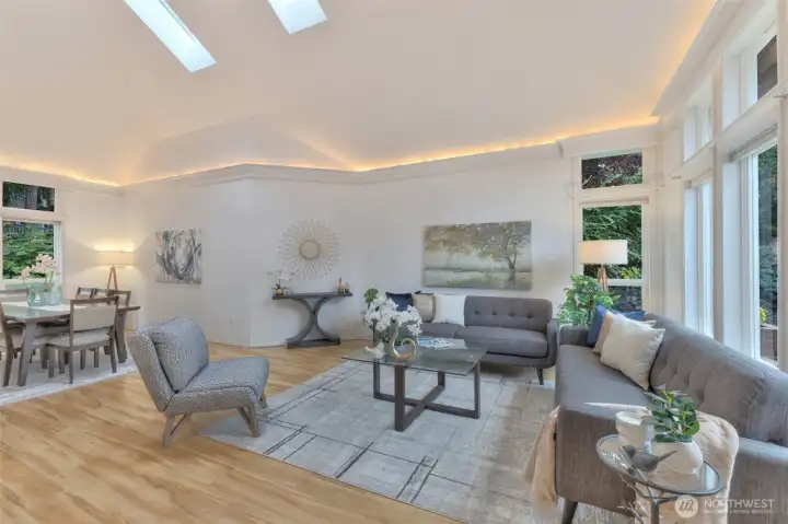 A large living room / dining room with vaulted ceilings, skylights, and cove lighting.