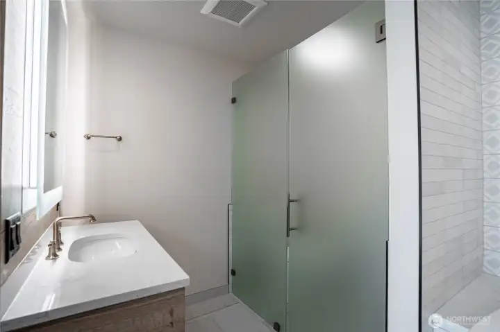 Twin bathroom sinks in the en suite primary bathroom with halo-illuminated mirrors and separate toilet area with privacy glass doors.