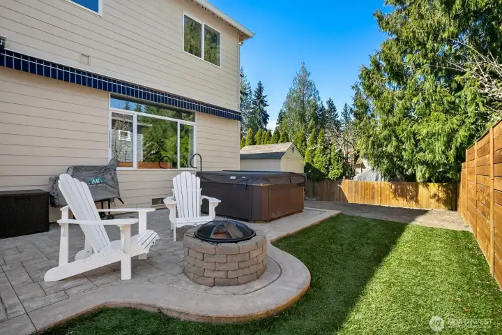 Backyard showing fire pit, hot tub (conveys with sale), storage shed, and area for potential gardening.