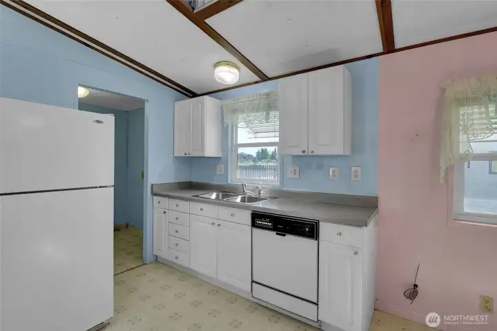 The kitchen has such soft and calming colors especially with the white against the blue.  Here you see this kitchen has a fridge and dishwasher along with a fine looking double sink!