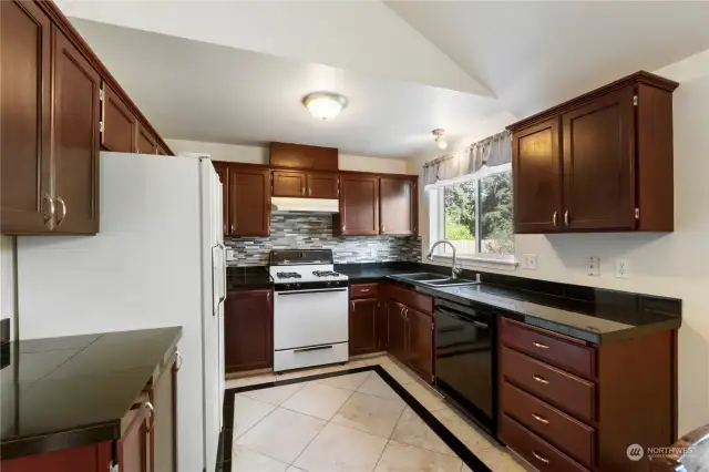 Beautiful kitchen offers tile counters, backsplash and flooring along with rich cherry cabinets.