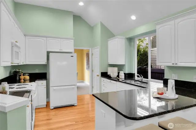 Light, bright kitchen with paneled white cabinets, shiny-brass hardware. Grocery pantry with paneled Quaker door, coated ventilated wire shelving. Oak-hardwood floor in kitchen extends into the breakfast area. Maytag® bottom freezer refrigerator. Upgraded countertops with full bullnose finished edges. GE® range-oven with GE® Spacemaker XL microwave oven above. Kenmore® dishwasher. Undermounted stainless-steel double sinks with In-Sink-Erator® food waste disposal, brushed-nickel faucet, big window for natural light. Vaulted ceiling with recessed lighting.