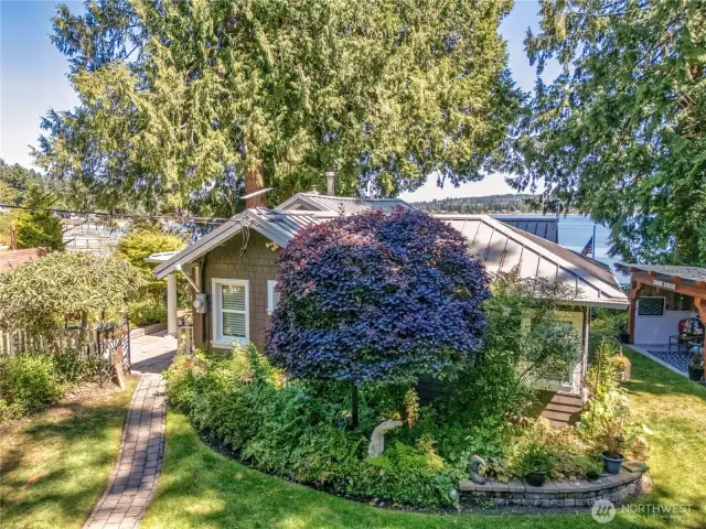 Lush mature landscaping surrounds the property with blooming shrubs, vibrant perennials, and towering trees creating a sense of privacy and timeless beauty.
