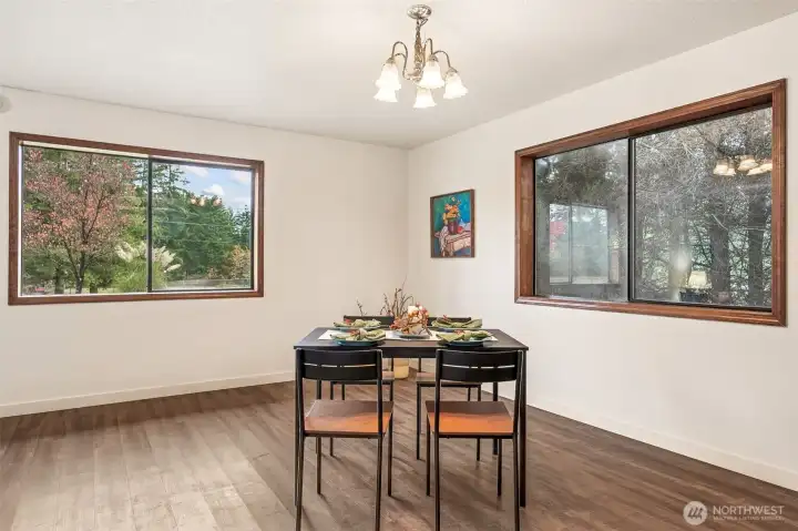 Two large picture windows bring the outdoors in and frame the serene grounds created by privacy trees .  The la ample corner might be the perfect place for your future wood or propane freestanding stove or display cabinet.