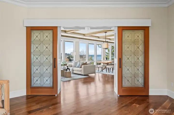 A breathtaking transition. Two massive sliding glass doors dissolve the boundaries between the foyer and the living spaces, immediately drawing your eye to the shimmering waterfront vistas beyond.
