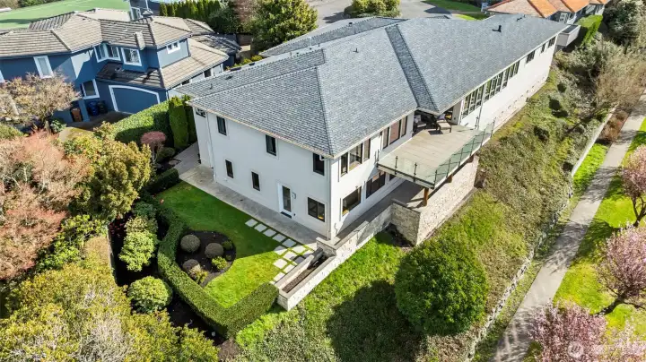 This perspective showcases the seamless vertical integration of the home. The upper-level patio deck offers an elevated vantage point over the manicured stone terrace and the vibrant cherry blossom path below.