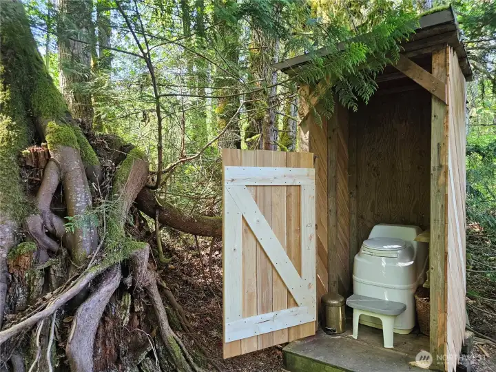 An adorable outdoor composting toilet is centrally located.