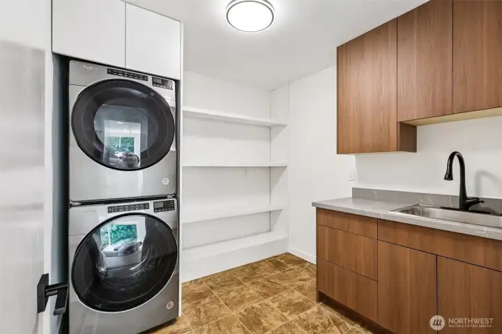 The updated laundry room includes a utility sink, built-in cabinetry and open shelving.