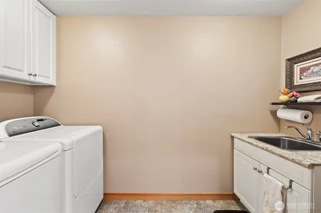 The updated laundry room features a side-by-side washer and dryer, a utility sink, and cabinets for extra storage space.