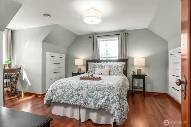Upstairs primary suite offers a private sanctuary with soft sage colored walls, coved ceilings, and rich refinished hardwood flooring and dual custom built-in dressers
