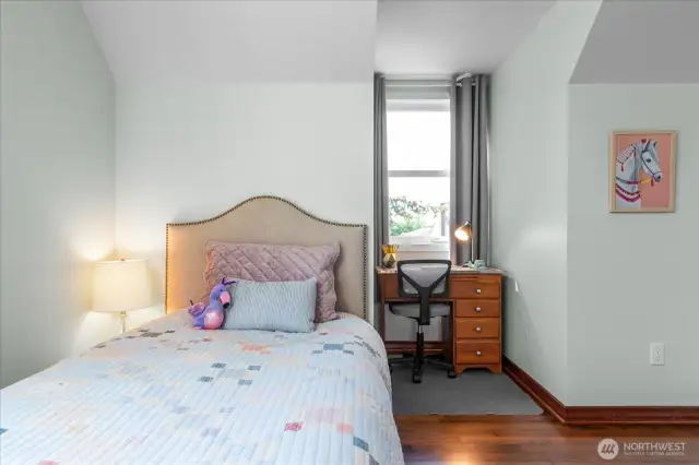 A room with a whimsical feel, this upstairs secondary bedroom offers space for two twin beds and desk alcove offering birds-eye neighborhood views