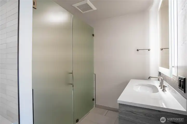 Twin bathroom sinks in the en suite primary bathroom with halo-illuminated mirrors and separate toilet area with privacy glass doors.