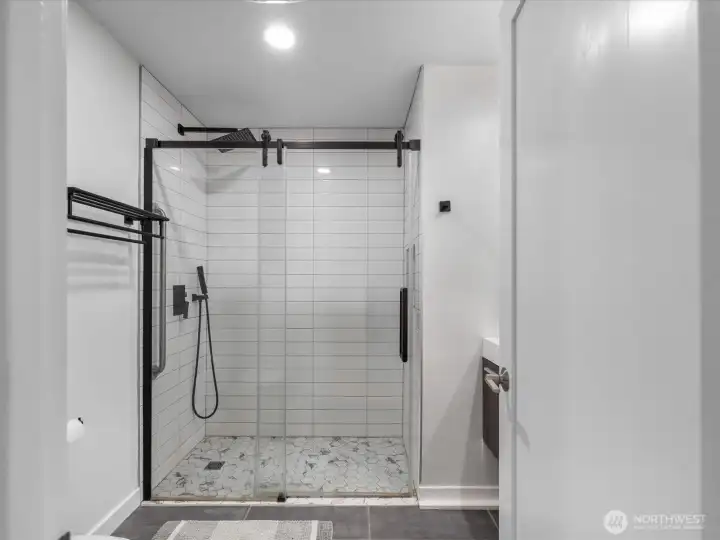 A spa-like updated hall bathroom featuring walk-in shower, with designer pebble tile flooring sleek matte black hardware double sinks for a modern, high-end finish.