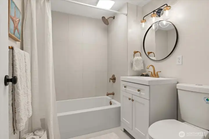 Elegant, tiled floors and tub surround, accented with warm brushed gold fixtures feel both timeless and tasteful in the lower level remodeled bath
