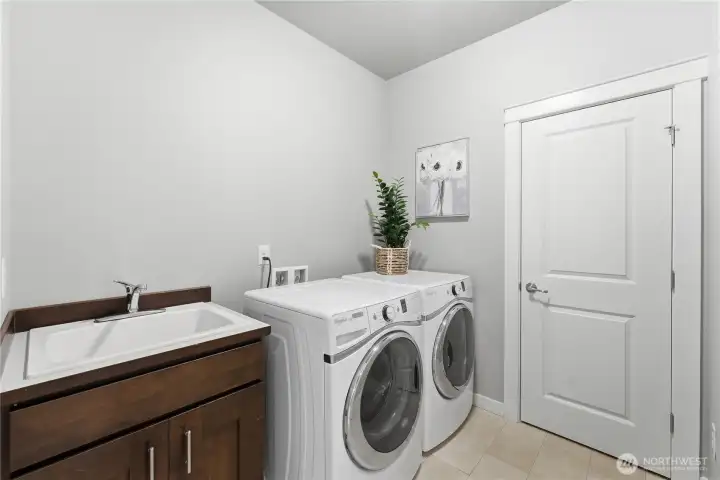 A well-appointed second floor laundry with a sink and newer washer and dryer that stay. The adjacent door opens to the media closet housing the on-Q wiring system and internet setup